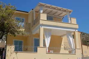 Un immeuble de deux étages doté de balcons, de rideaux blancs et de volets bleus.