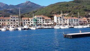 Ein Yachthafen mit vertäuten Booten, Gebäude mit roten Dächern und ein Berg im Hintergrund.