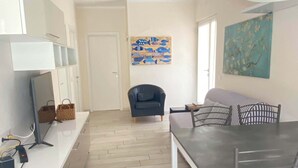 Een moderne woonkamer met een eettafel, een bank en een televisie. Twee schilderijen hangen aan de muur en er is een deur te zien op de achtergrond.