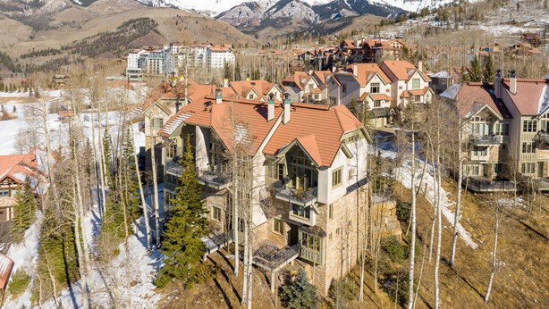 A residential area with houses featuring red-tiled roofs and stone facades, surrounded by snow-covered mountains and sparse trees. - Classic Aspen Ridge Home by InvitedHome | Walk to Ski and Core, Wilson Views (Mountain Village)