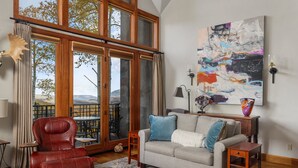 A living room with a red leather chair, a grey sofa, a large abstract painting, and a view through large windows. - Classic Aspen Ridge Home by InvitedHome | Walk to Ski and Core, Wilson Views (Mountain Village)