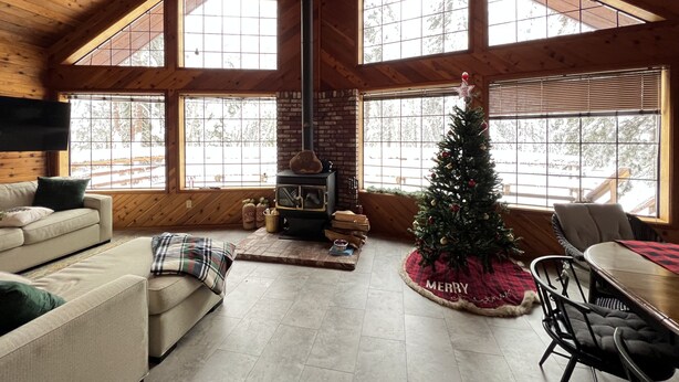 A cozy cabin interior with a fireplace, a Christmas tree, and a large window overlooking a snowy landscape. - Little Bear Lodge Ponderosa Ca (Springville)