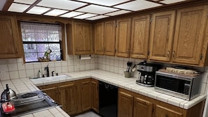 A kitchen with wooden cabinets, a tiled backsplash, a stove, a microwave, and a window with a view of the outdoors. - Little Bear Lodge Ponderosa Ca (Springville)