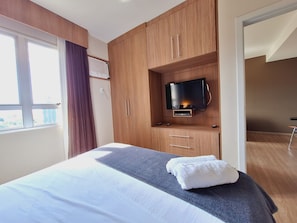 Habitación de hotel con cama, televisor montado en un mueble de madera y ventana con cortinas.