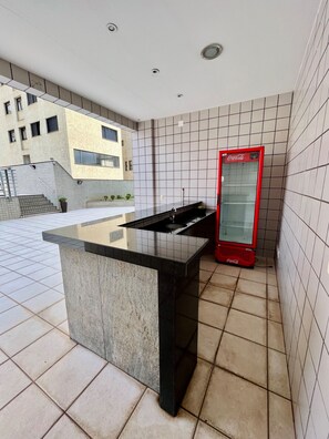 Una cocina moderna con encimera negra, refrigerador rojo de Coca-Cola y piso de baldosas.