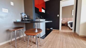A compact kitchen with a dining area, a coffee machine, and a small trash bin.