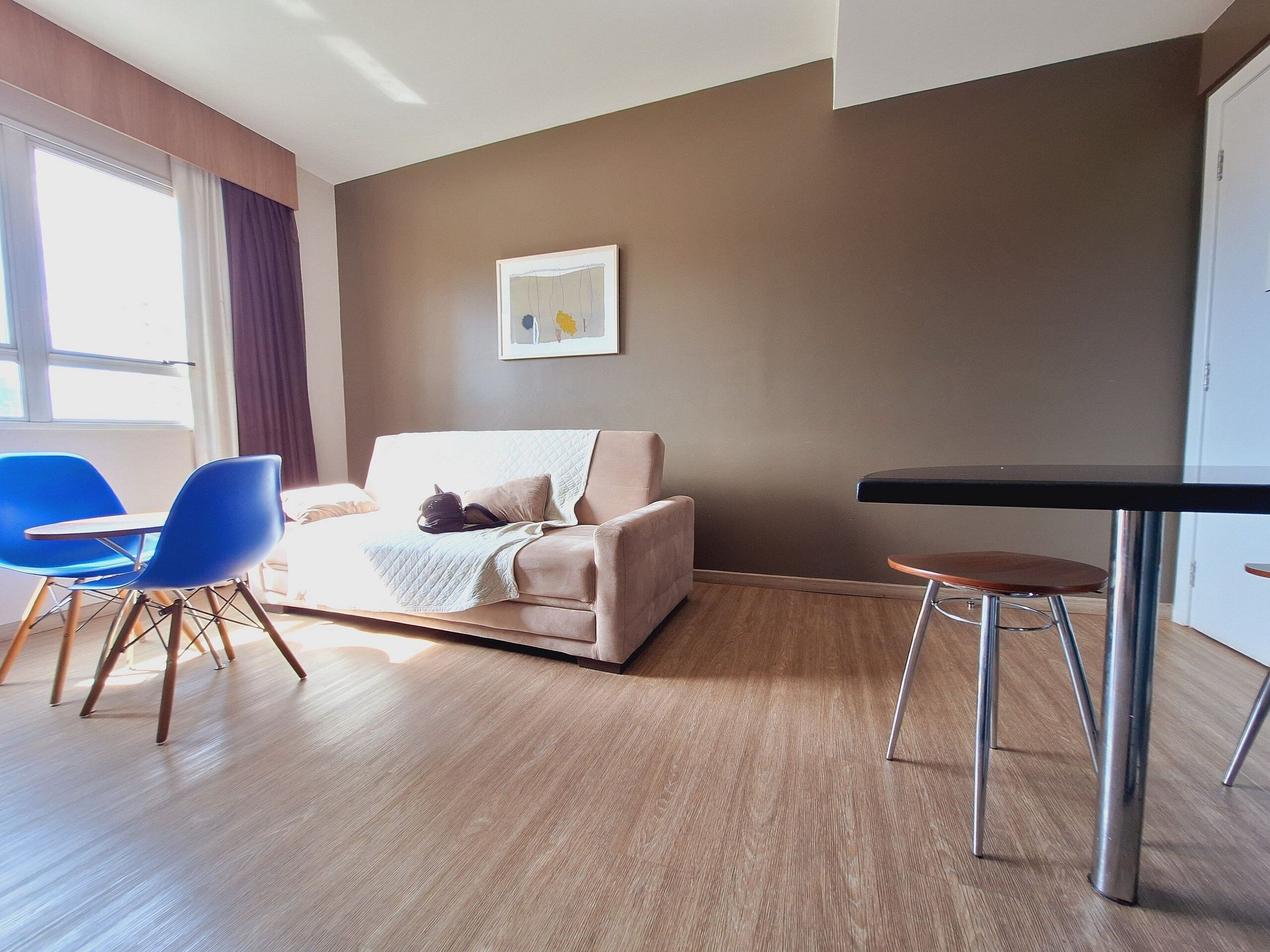 A modern living room with a beige sofa, blue chairs, a small table, and a framed picture on the wall.