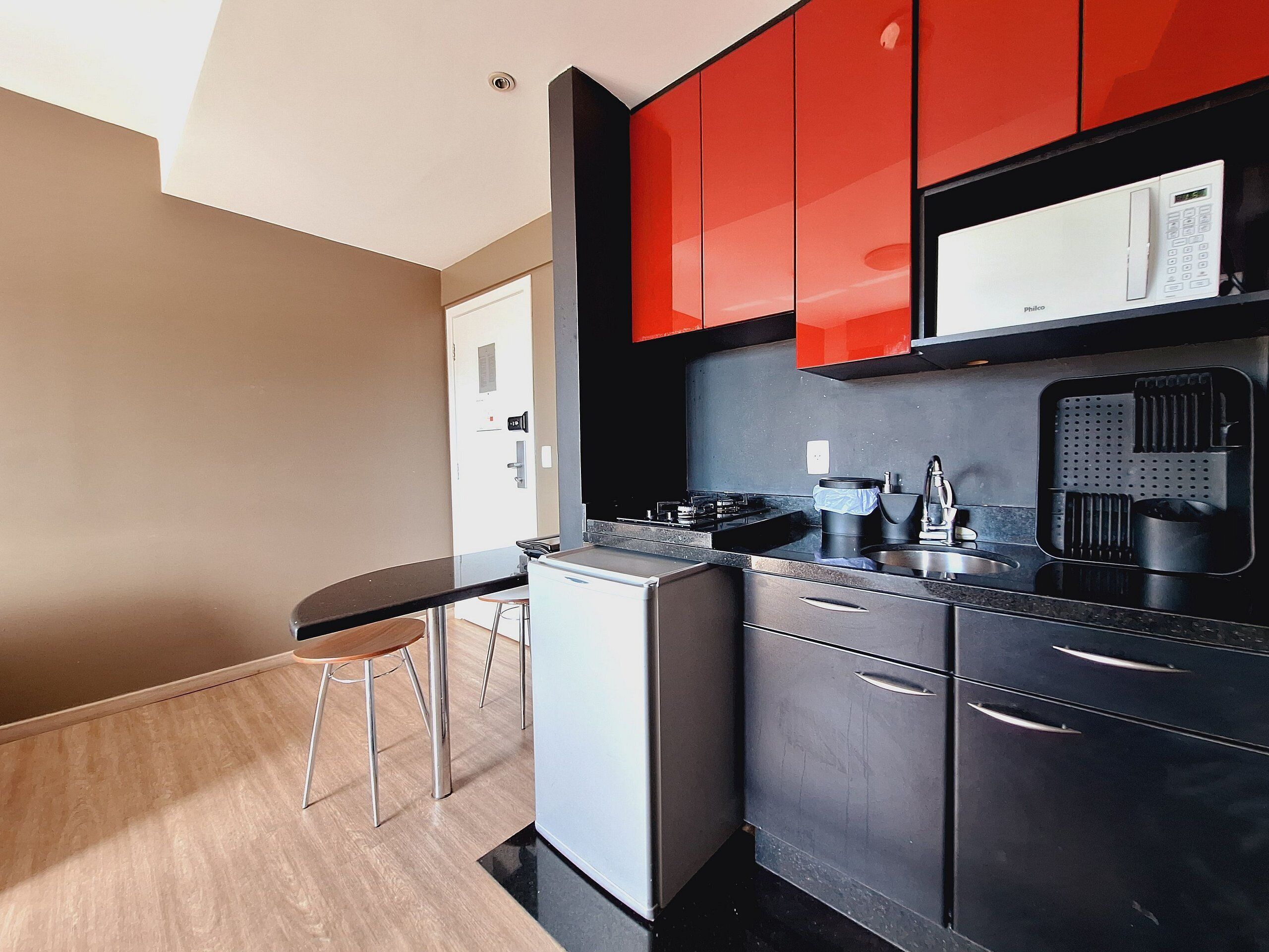 Una cocina moderna con armarios rojos, encimera negra y lavadora-secadora compacta.