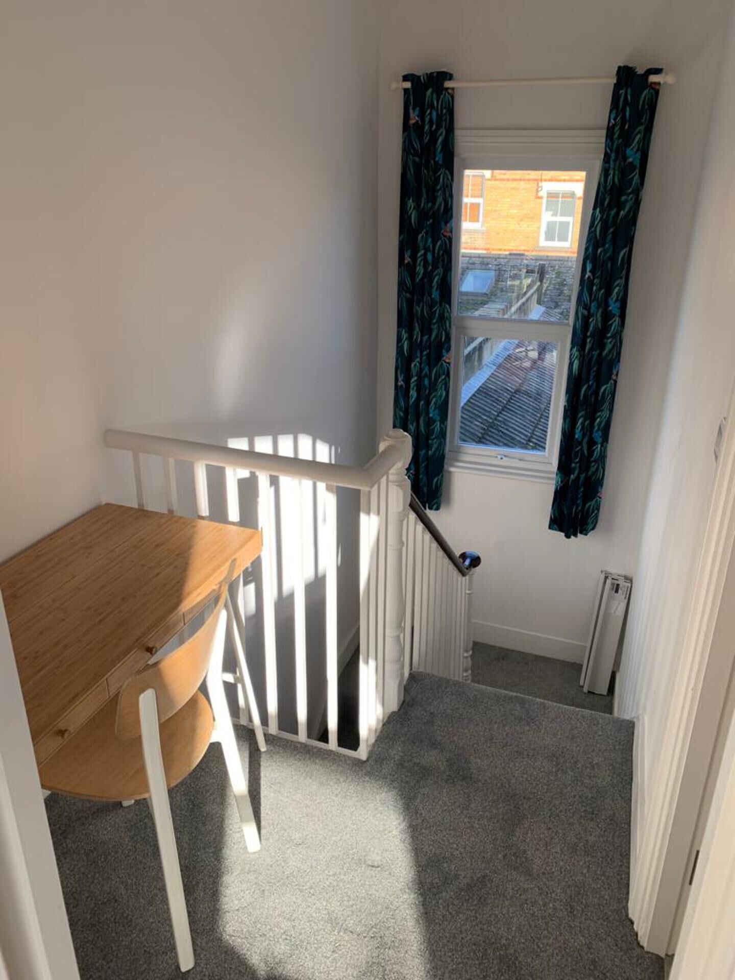 A small room with a wooden desk, a white radiator, and a window with curtains.