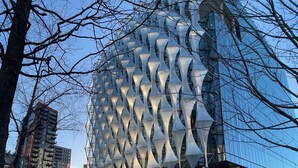 Un edificio moderno con una fachada geométrica distintiva, rodeado de árboles y otros edificios.