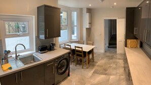 Una cocina moderna con lavadora integrada, un comedor con mesa y sillas, y vistas al exterior a través de amplios ventanales.