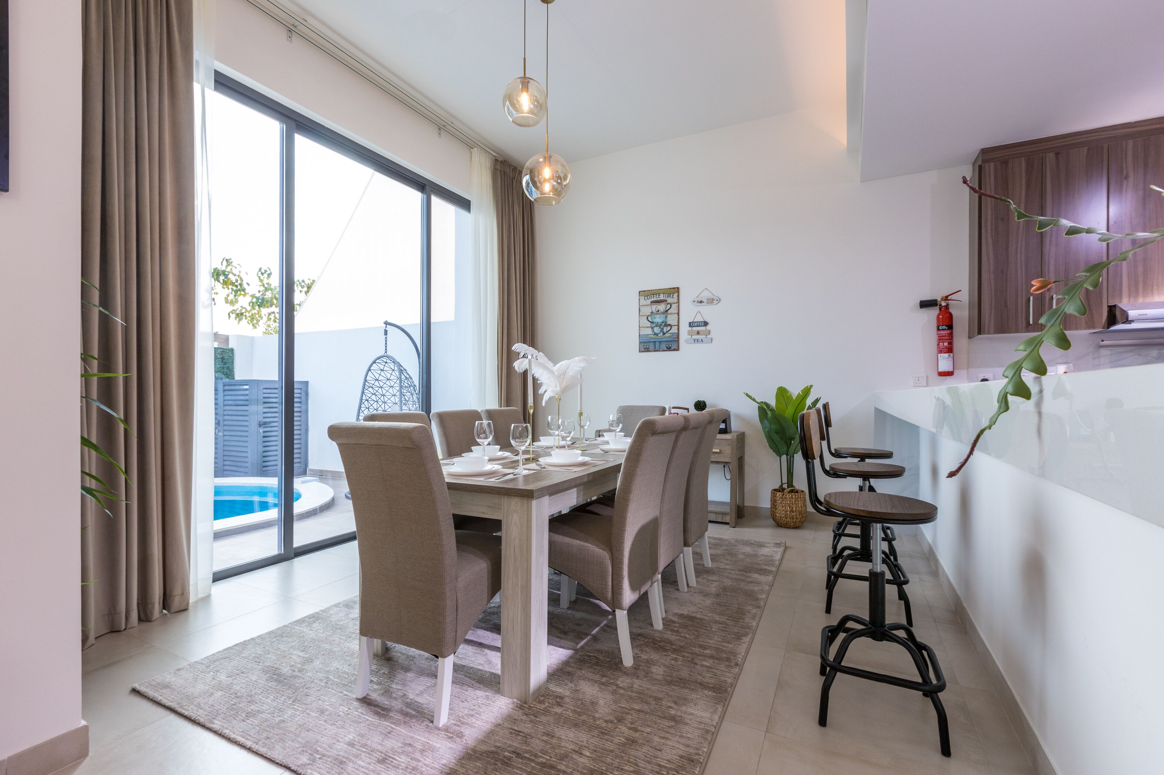 Un espace repas avec une table dressée pour quatre personnes, un coin bar avec des tabourets et une vue sur une piscine.