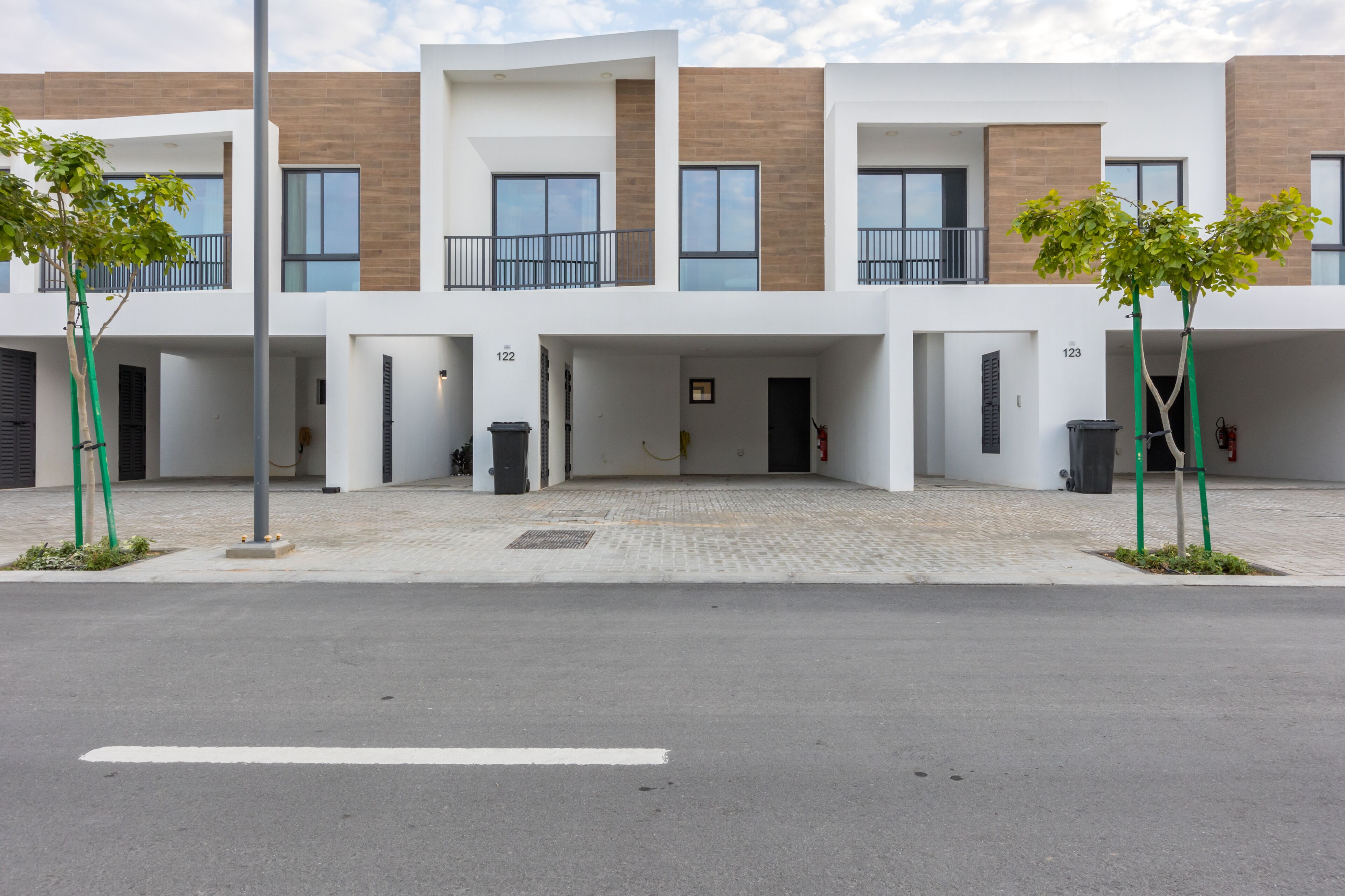 A modern multi-story residential building with a clean, minimalist design, featuring balconies and a paved entrance area.