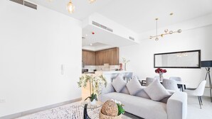 A modern living room with a sofa, a coffee table, and a dining area with chairs and a table. - Nasma Luxury Stays- Ras Al Khaimah (Ras Al Khaimah)
