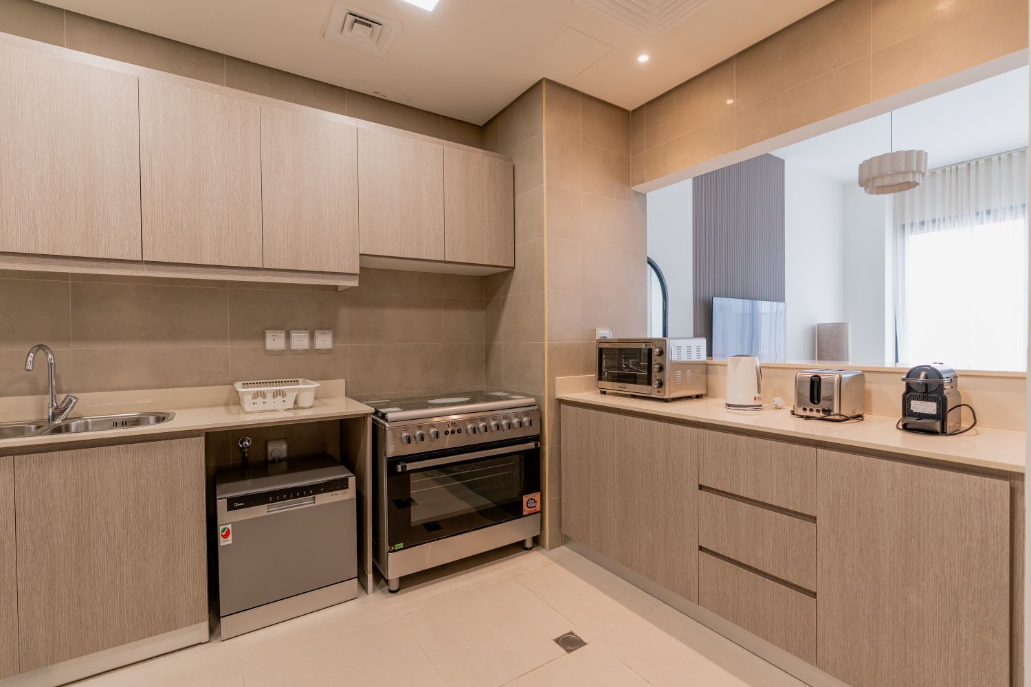 A modern kitchen with light wood cabinets, stainless steel appliances, and a window providing natural light.