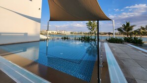 A swimming pool with a clear view of the sea and buildings in the background. - Nasma Luxury Stays- Ras Al Khaimah (Ras Al Khaimah)