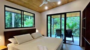 Une chambre moderne avec un grand lit, un plafond en bois et de grandes fenêtres donnant sur un paysage verdoyant.