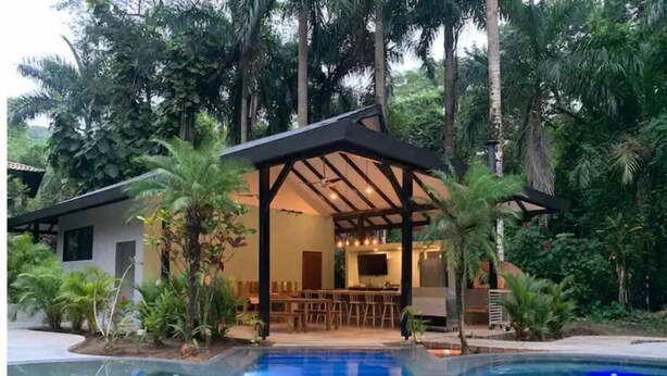 Un espace aménagé au bord de la piscine, comprenant un coin salon couvert, un bar et une piscine.