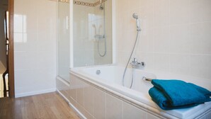 A bathroom with a glass-enclosed shower, a bathtub with a blue towel, and white tiled walls. - Spacious vacation home 5 min steps from city center. (Brugge)