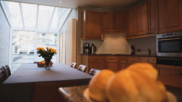 A modern kitchen with wooden cabinets, a dining table with chairs, and a large window. - Spacious vacation home 5 min steps from city center. (Brugge)