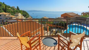 Un balcone con vista sul mare, una piscina e sedie di legno.