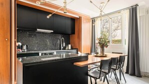 A modern kitchen with black cabinets, a granite countertop, and a central island. There is a dining area with a wooden table and black chairs. - Eiffel Tower - 4 bedrooms Air Conditioning (Paris)