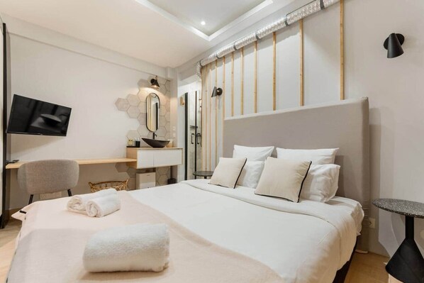Una habitación de hotel moderna con una cama grande, un escritorio, una silla, un televisor y un baño con ducha e inodoro.