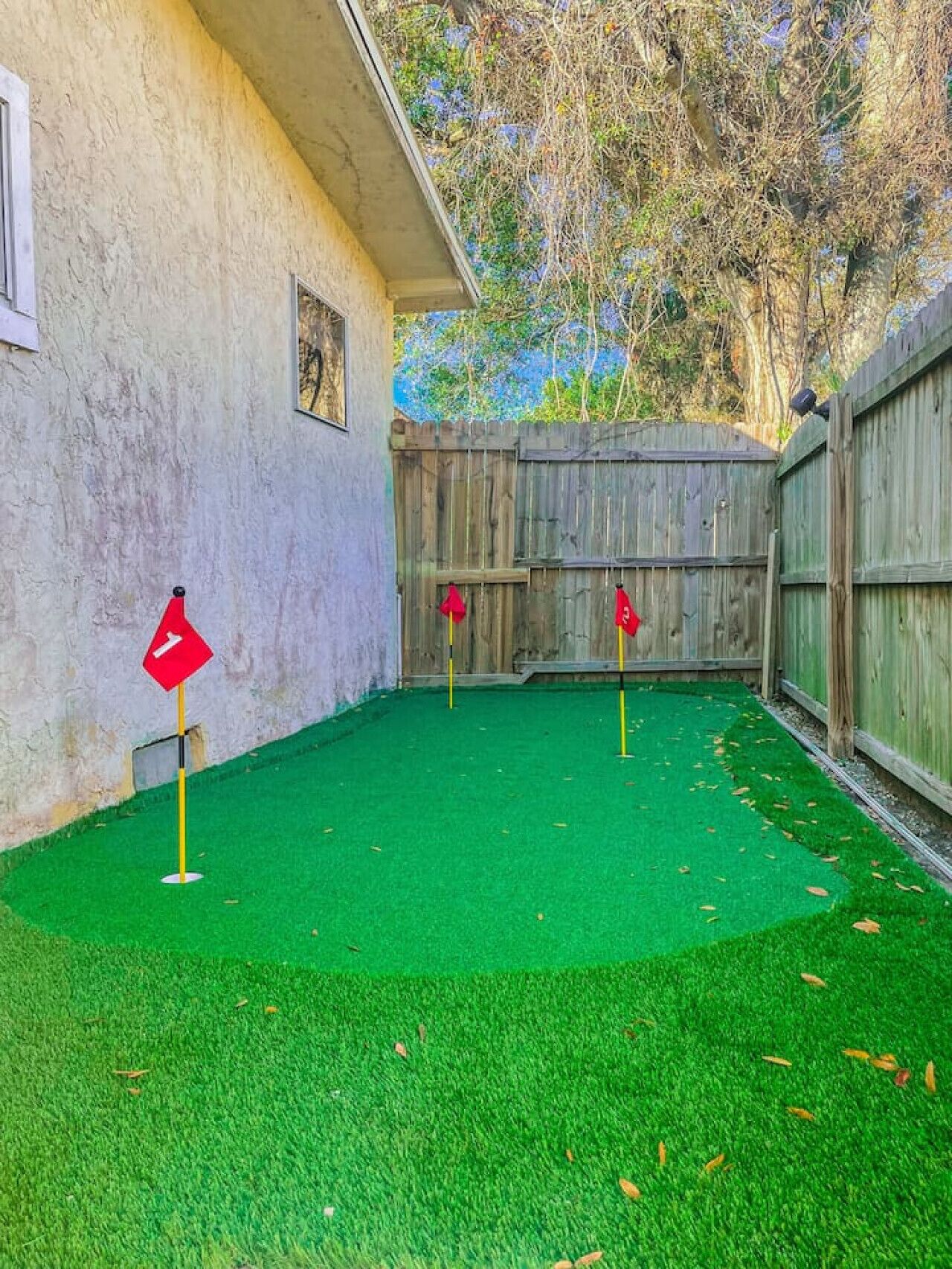 A backyard with artificial green turf, a wooden fence, and three red flags.