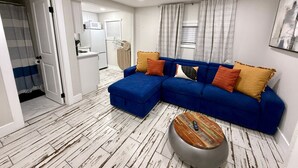 Een moderne woonkamer met een blauwe hoekbank, een ronde salontafel en een witte keuken op de achtergrond.