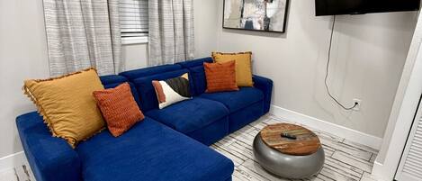 A modern living room with a blue sectional sofa, a round wooden coffee table, and a large abstract painting on the wall.