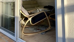 A room with a sliding glass door, a beige sofa, two rocking chairs, a small table, and a ceiling fan.