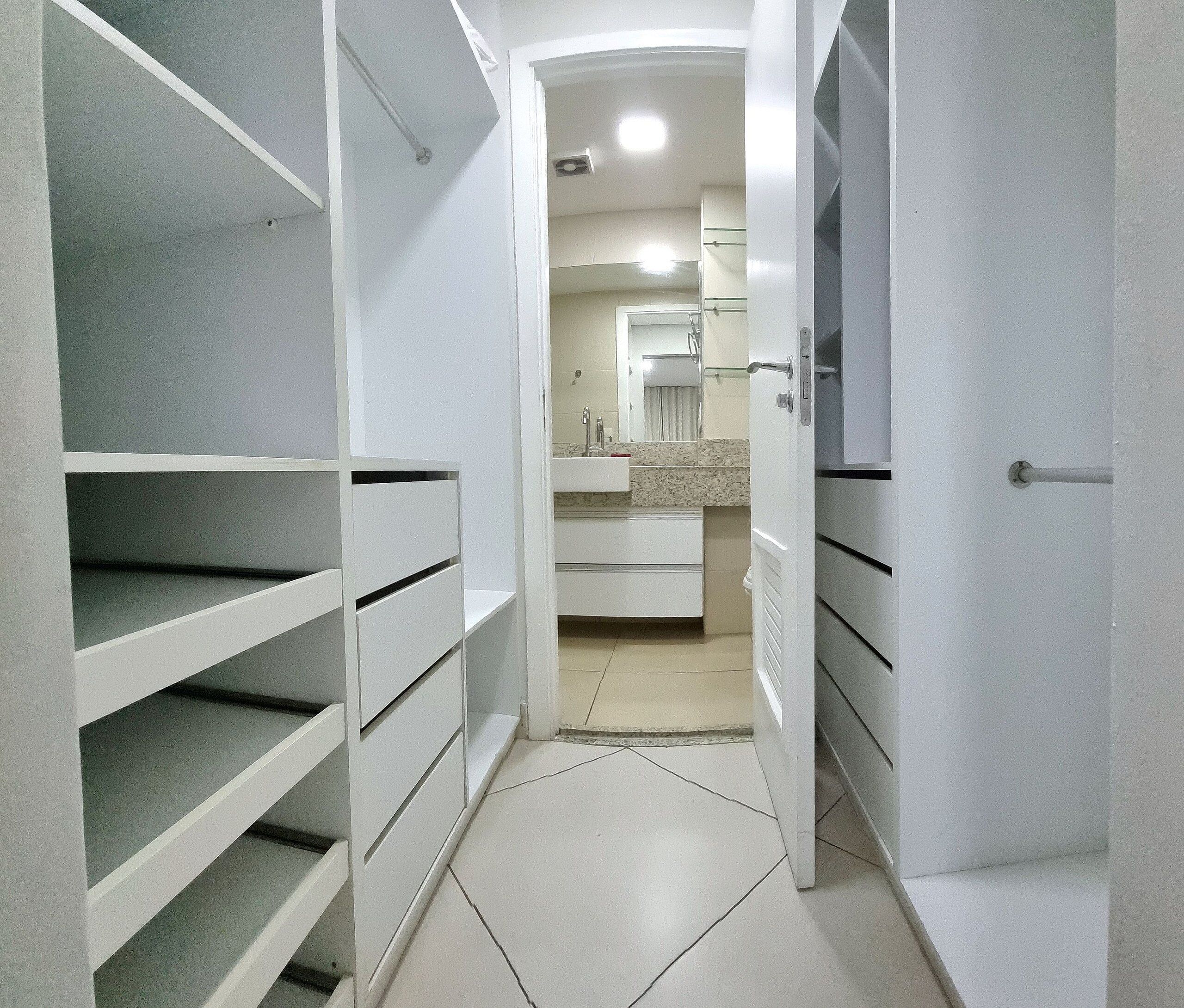 Un pasillo estrecho con armarios blancos a ambos lados y un baño al final.