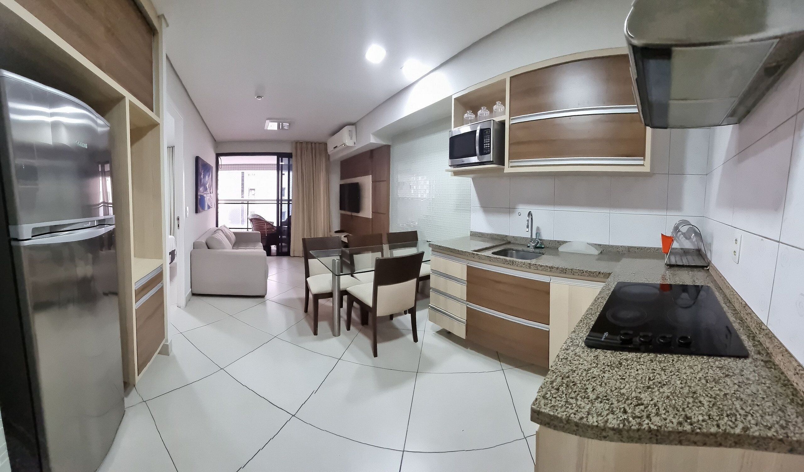 A modern kitchen with a built-in microwave, a stove, and a sink. There is a dining area with a table and chairs, and a sofa in the background.