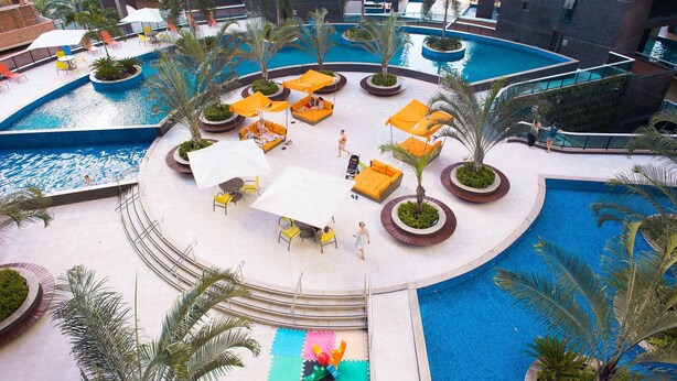 Area piscina sul tetto con diverse zone relax, palme e una fontana centrale.