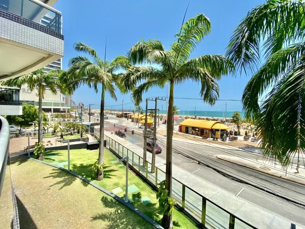 Una zona costiera urbana con palme, una linea tramviaria e un edificio con tetto giallo.
