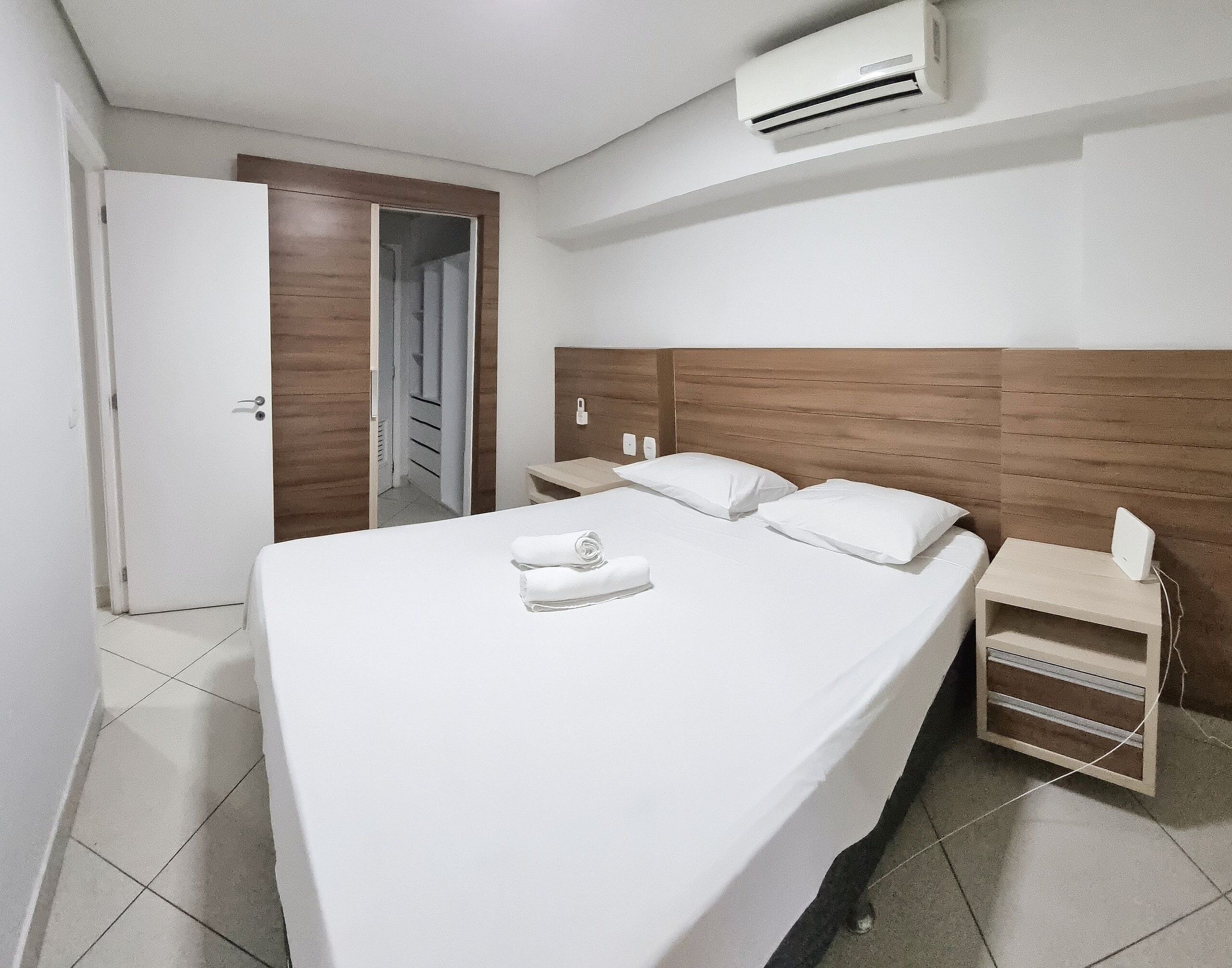 Hotellihuone, jossa on suuri sänky, yöpöytä, ilmastointilaite ja ovi, joka johtaa käytävään.