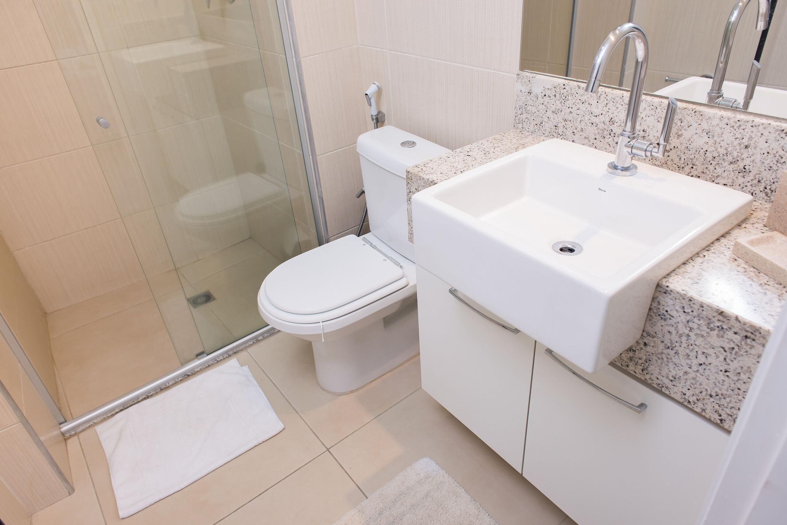 Un baño moderno con cabina de ducha de vidrio, inodoro blanco, lavamanos con encimera de granito y un espejo sobre el lavamanos.
