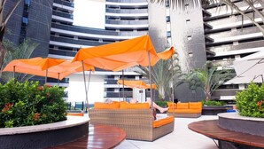 Un'area relax moderna all'aperto con mobili in vimini e ombrelloni arancioni, circondata da piante e architettura contemporanea.