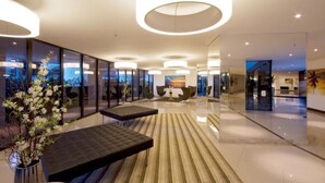 Una hall moderna con pareti in vetro, una zona salotto centrale e luci a soffitto circolari.