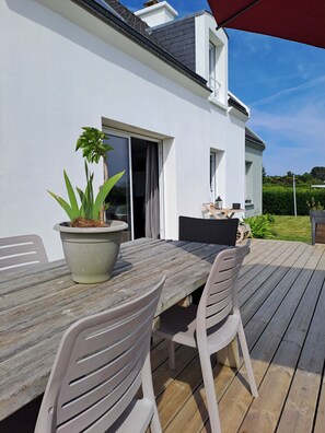 Eine Terrasse mit einem Holztisch, Stühlen, einem Blumentopf und einem roten Sonnenschirm.