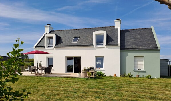 Ein zweistöckiges Haus mit Terrasse, einem roten Sonnenschirm und Topfpflanzen.