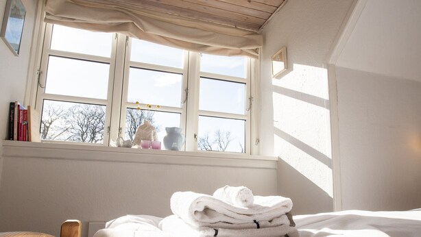 Un dormitorio con cama, ventana con cortinas y vistas a árboles desde afuera.