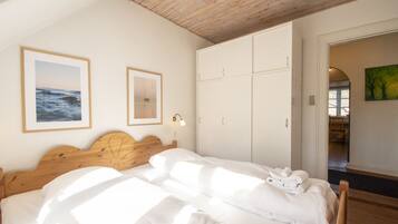 Un dormitorio con cabecera de madera, una cama con sábanas blancas, un armario y dos cuadros en la pared.