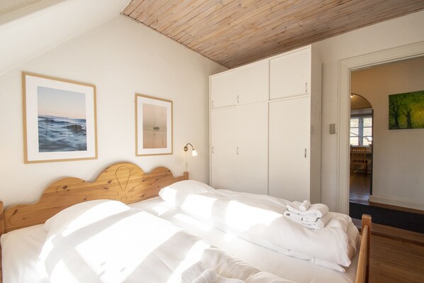 A bedroom with a wooden headboard, a bed with white linens, a wardrobe, and two framed pictures on the wall. - Guesthouse on the Danish German border (Krusaa)