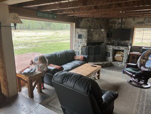 Cozy seating area with a fireplace, leather sofa, and armchair, offering a view of the outdoors.