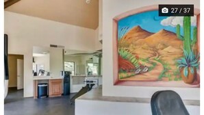 A spacious living area with a kitchen in the background, a large painting of a desert landscape on the wall, and a black chair in the foreground. - Luxury 2B 2B@ Catalina Foothills Resort - Tucson (Tucson)