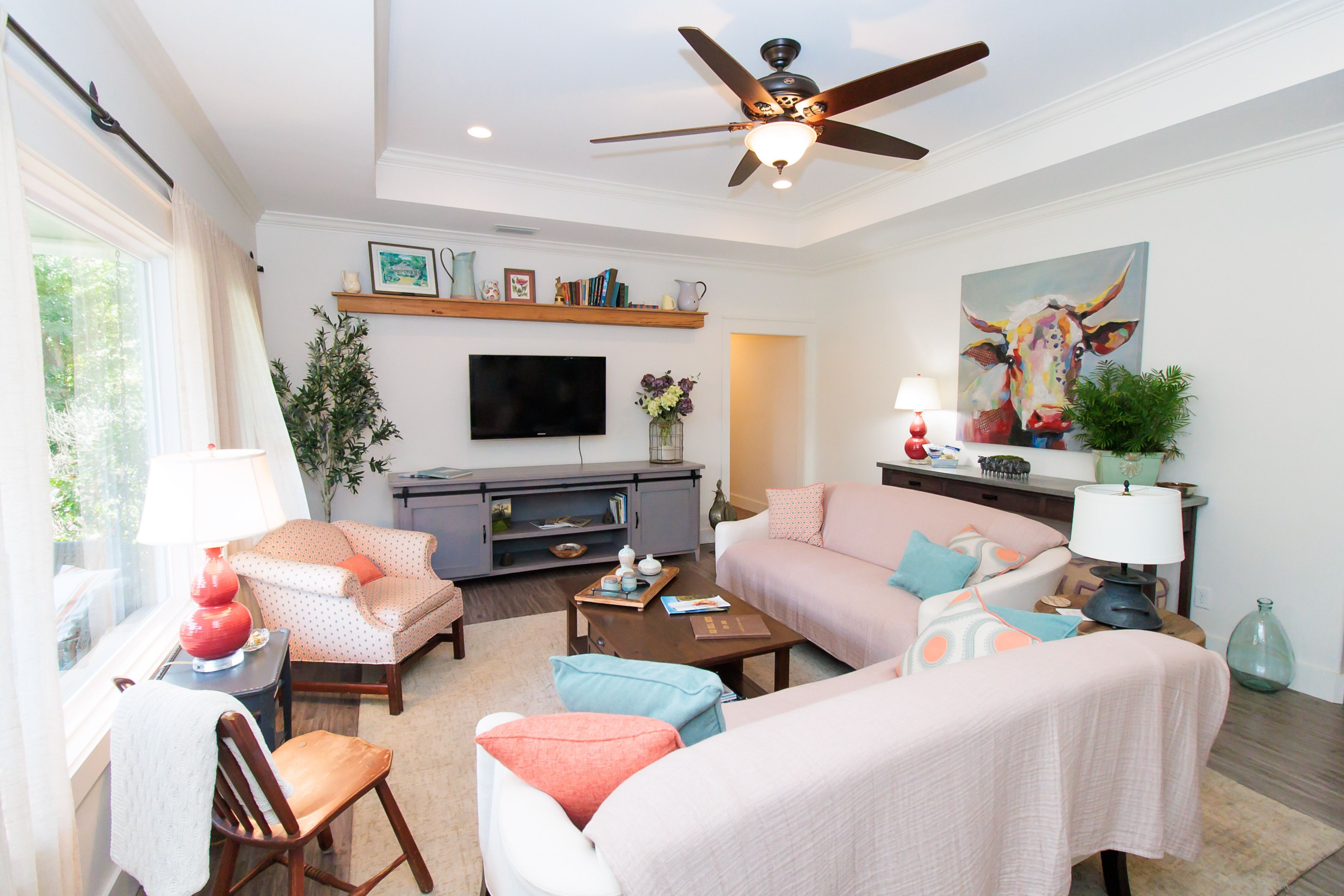 A living room with a ceiling fan, a flat-screen TV, and a sofa set.