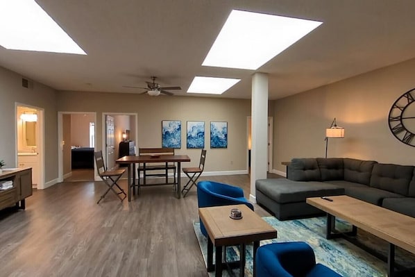 A spacious living room with a dining area, a ceiling fan, and artwork on the walls.