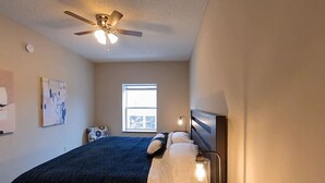 Ein Schlafzimmer mit Bett, Deckenventilator, Fenster und Wandleuchte.
