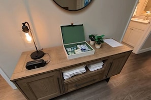 A wooden vanity with a green box containing toiletries, a lamp, and a potted plant.